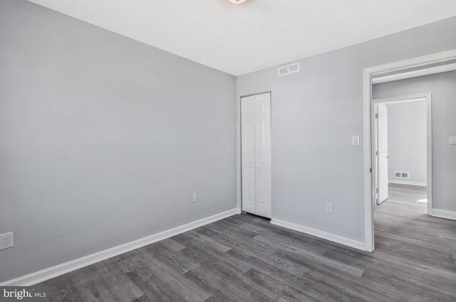 unfurnished bedroom with dark wood-style floors, a closet, visible vents, and baseboards