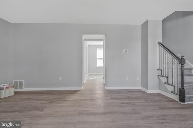 empty room with light wood-style floors, baseboards, stairs, and visible vents