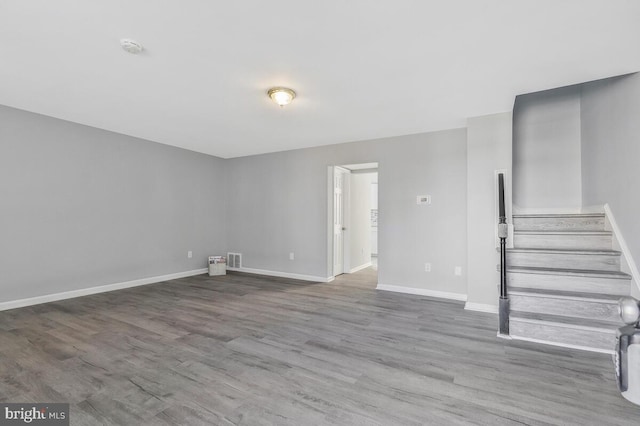 unfurnished living room with visible vents, stairway, baseboards, and wood finished floors