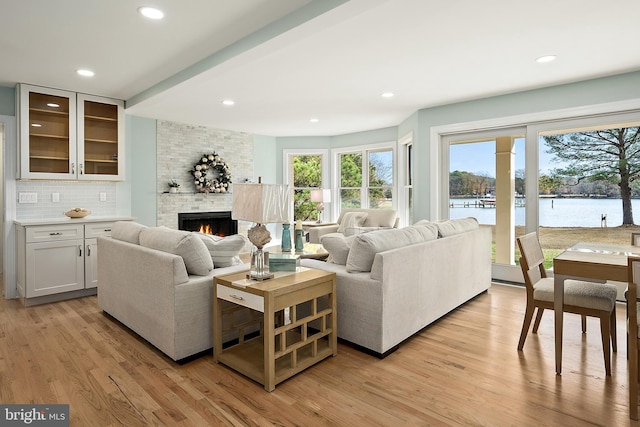 living room with a fireplace, a water view, a healthy amount of sunlight, and light hardwood / wood-style flooring