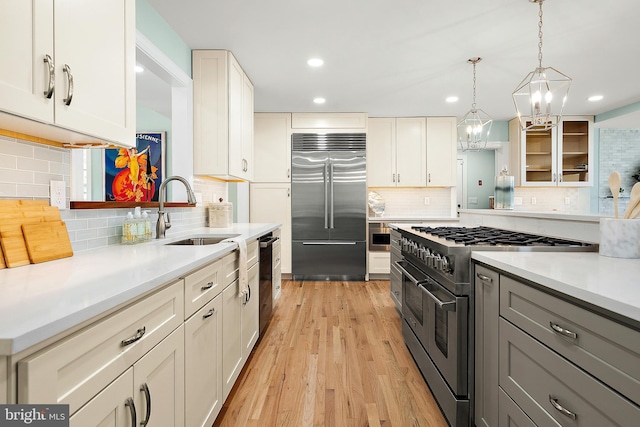 kitchen featuring sink, high quality appliances, white cabinets, light hardwood / wood-style floors, and hanging light fixtures