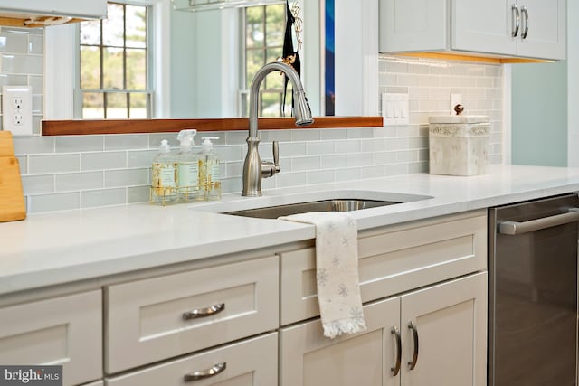 interior details with tasteful backsplash, sink, white cabinets, and stainless steel dishwasher