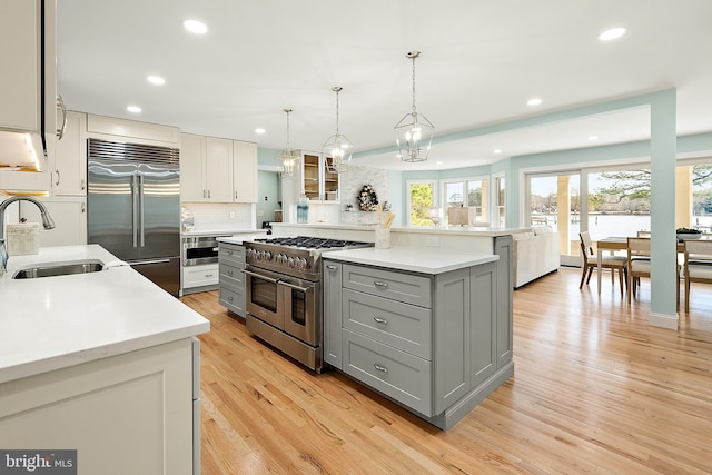 kitchen with gray cabinetry, sink, hanging light fixtures, high quality appliances, and light wood-type flooring