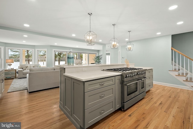 kitchen featuring gray cabinetry, range with two ovens, light hardwood / wood-style floors, a kitchen island, and hanging light fixtures