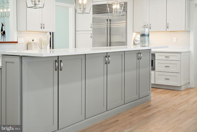 kitchen with tasteful backsplash, built in refrigerator, pendant lighting, and light wood-type flooring