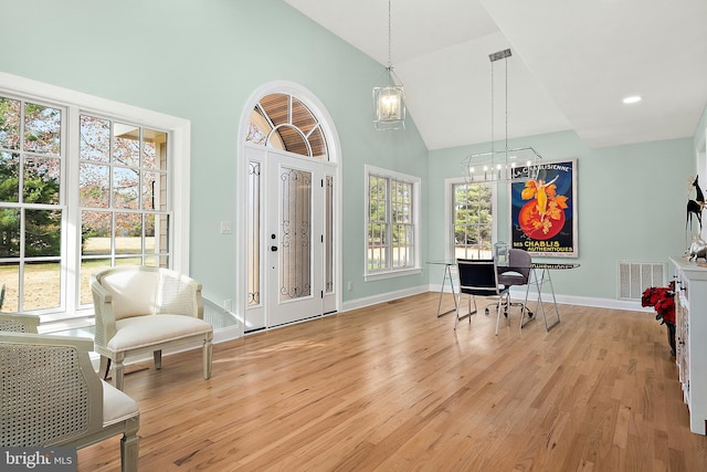 interior space with a healthy amount of sunlight, light hardwood / wood-style floors, high vaulted ceiling, and a chandelier