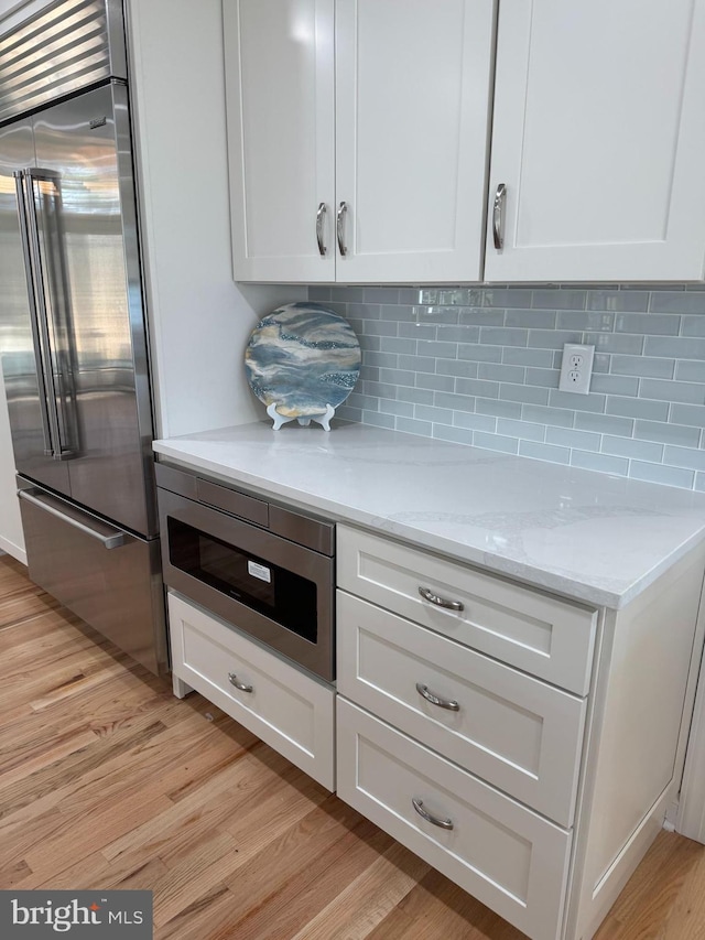 kitchen featuring light wood-type flooring, built in appliances, white cabinets, and light stone counters