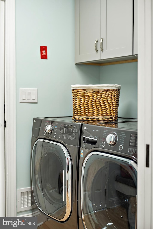 clothes washing area with washer and dryer and cabinets