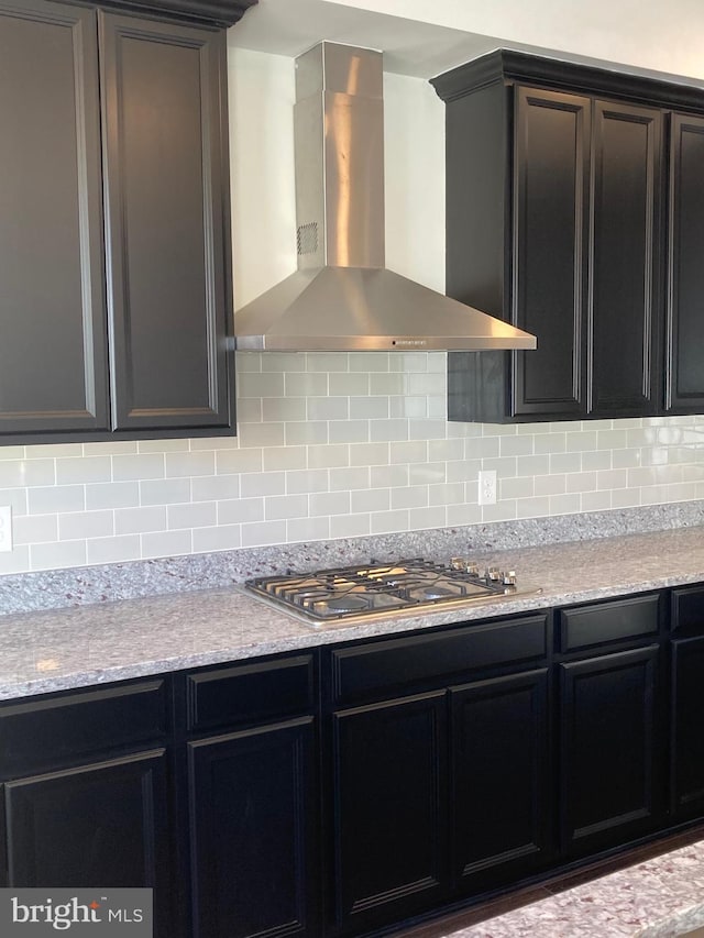 kitchen featuring tasteful backsplash, light stone counters, wall chimney range hood, and stainless steel gas cooktop