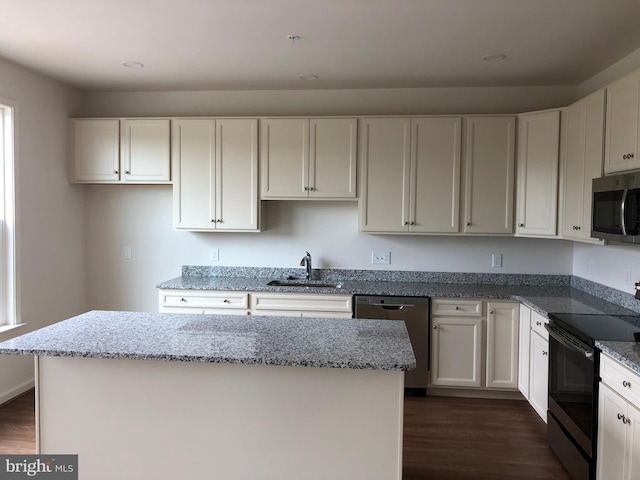 kitchen featuring a center island, sink, appliances with stainless steel finishes, light stone counters, and white cabinetry