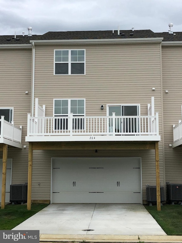 rear view of house featuring a balcony, central AC unit, and a garage