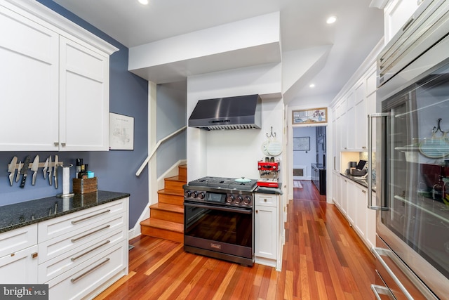 kitchen with white cabinets, wall chimney exhaust hood, stainless steel stove, and light wood-type flooring