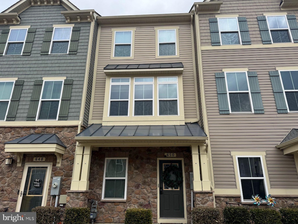 townhome / multi-family property featuring a standing seam roof, stone siding, and metal roof