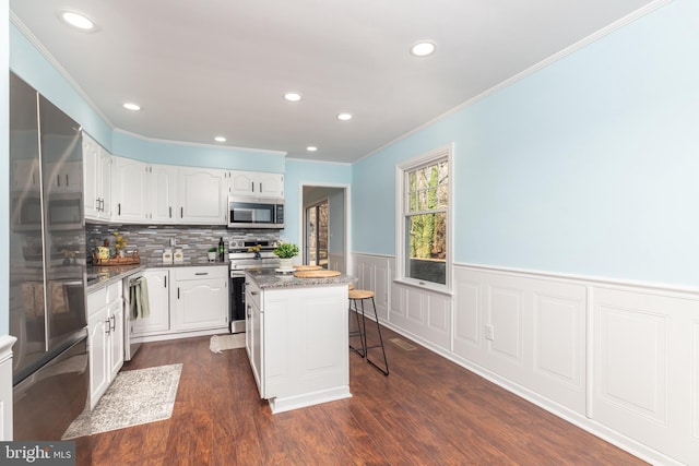 kitchen with a kitchen bar, appliances with stainless steel finishes, white cabinets, a center island, and dark hardwood / wood-style floors