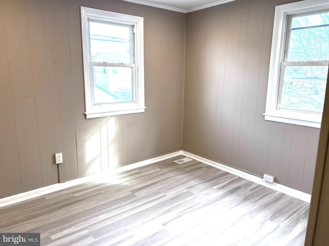 spare room with wood walls, light hardwood / wood-style flooring, and crown molding