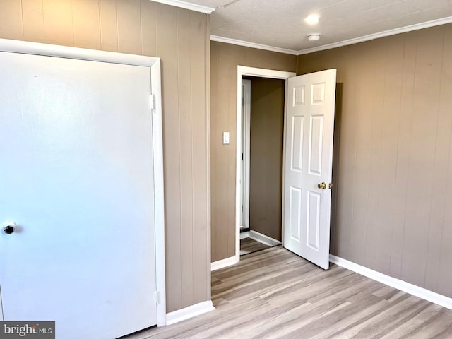 unfurnished bedroom with wood walls, ornamental molding, and light hardwood / wood-style flooring