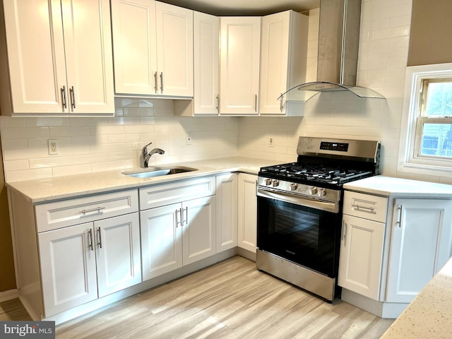 kitchen with white cabinets, gas stove, light hardwood / wood-style floors, and wall chimney range hood