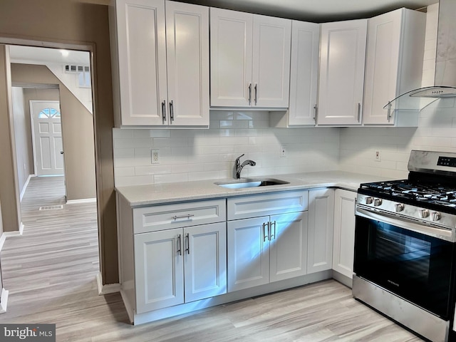 kitchen featuring white cabinetry, stainless steel gas stove, wall chimney exhaust hood, sink, and tasteful backsplash