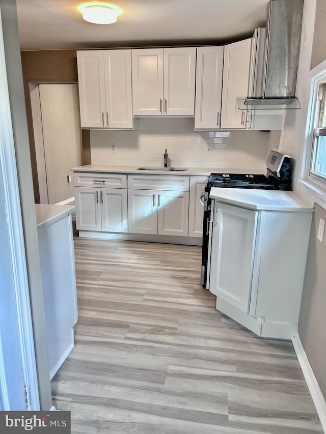 kitchen with white cabinets, wall chimney range hood, light wood-type flooring, tasteful backsplash, and range