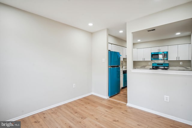 kitchen with white cabinetry, stove, fridge, and light hardwood / wood-style flooring