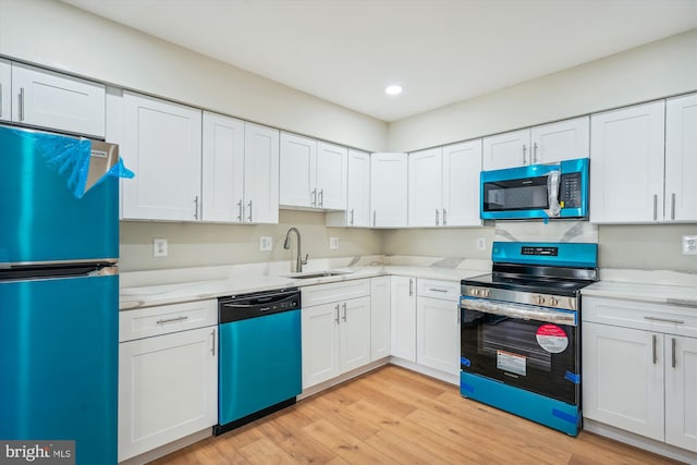 kitchen with appliances with stainless steel finishes, light stone counters, sink, light hardwood / wood-style floors, and white cabinetry