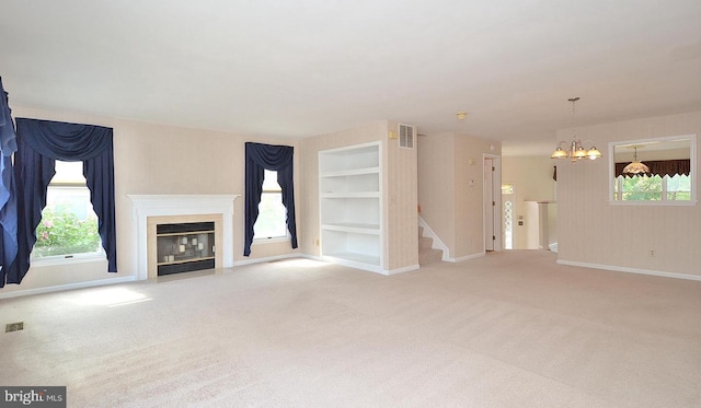 unfurnished living room featuring a chandelier, built in shelves, a wealth of natural light, and light carpet