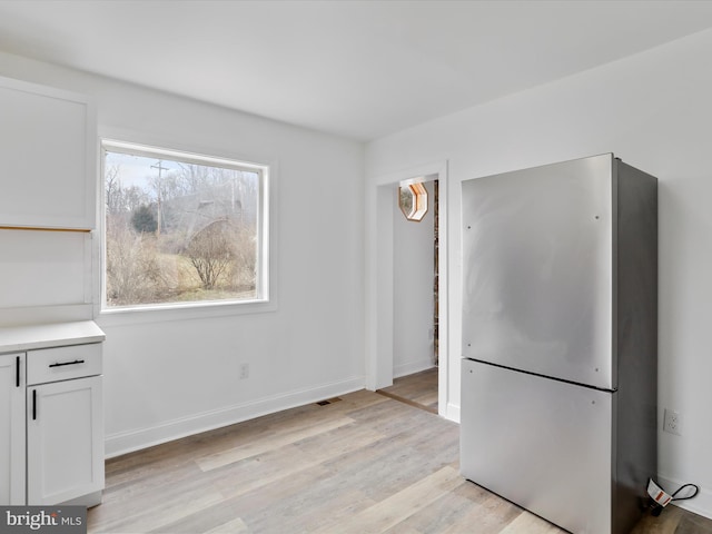 kitchen with white cabinets, stainless steel fridge, and light hardwood / wood-style flooring