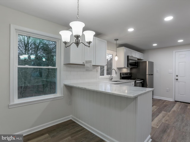 kitchen with hanging light fixtures, dark hardwood / wood-style floors, kitchen peninsula, white cabinets, and appliances with stainless steel finishes