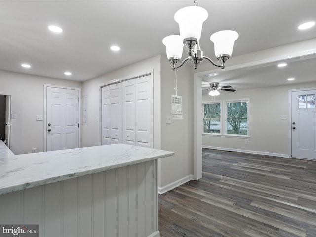 kitchen with light stone countertops, ceiling fan with notable chandelier, dark wood-type flooring, decorative light fixtures, and stainless steel refrigerator