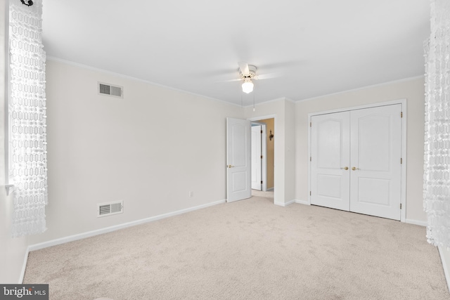 unfurnished bedroom featuring a closet, light colored carpet, ceiling fan, and ornamental molding