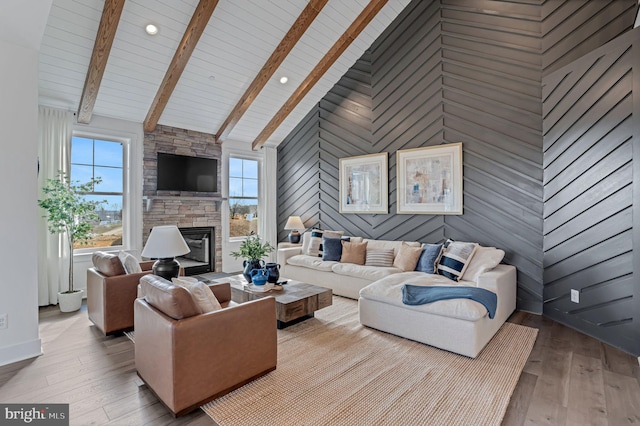 living room with wood walls, light hardwood / wood-style floors, a stone fireplace, and high vaulted ceiling