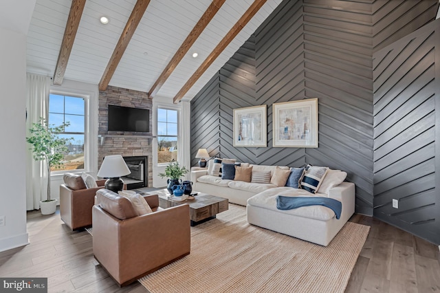 living room featuring wooden walls, a stone fireplace, light wood-type flooring, and high vaulted ceiling