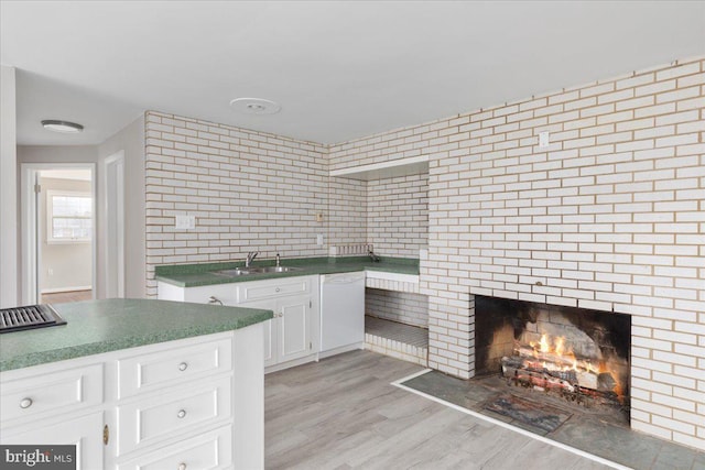 kitchen with dishwasher, white cabinets, sink, a brick fireplace, and light hardwood / wood-style flooring