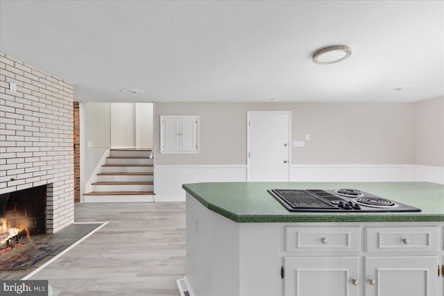 kitchen featuring white cabinets, stovetop, light wood-type flooring, and a fireplace