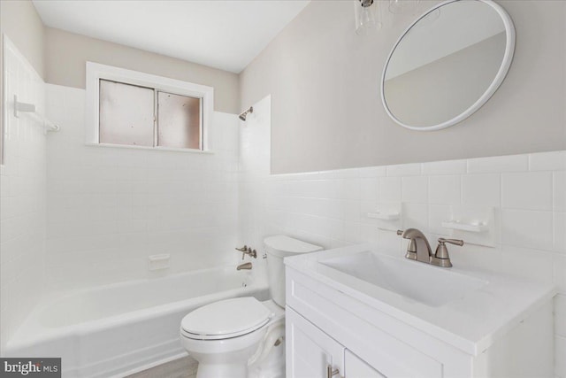 full bathroom with tiled shower / bath, vanity, toilet, and tile walls