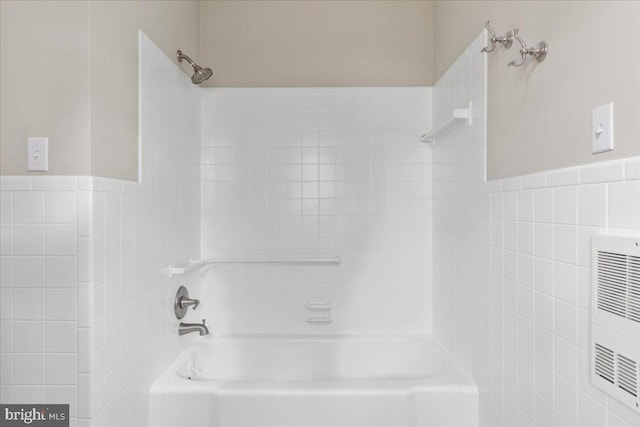 bathroom with heating unit, tiled shower / bath combo, and tile walls