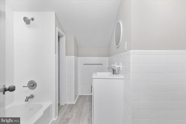 bathroom with hardwood / wood-style floors, vanity, tile walls, and tiled shower / bath