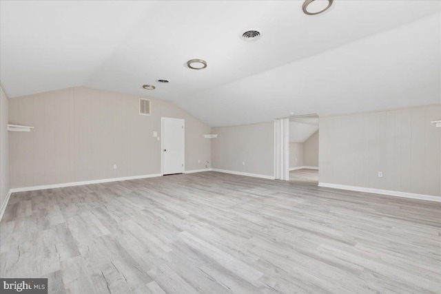 additional living space featuring wood walls, light hardwood / wood-style floors, and vaulted ceiling