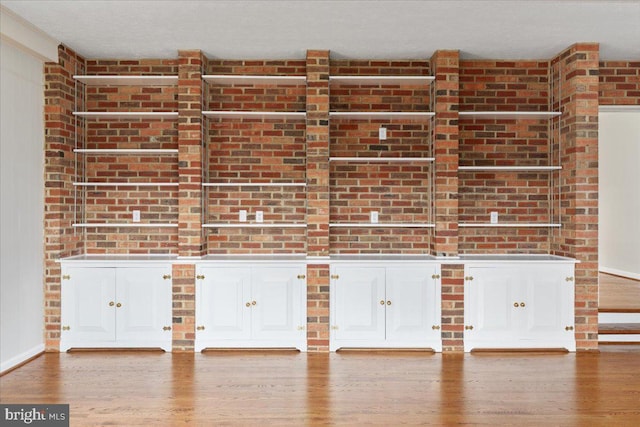 interior space with a textured ceiling, light wood-type flooring, and brick wall