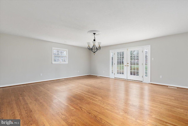 spare room with french doors, an inviting chandelier, and light hardwood / wood-style flooring