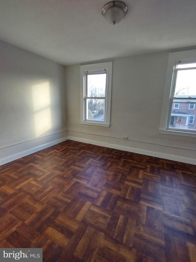 unfurnished room featuring dark parquet flooring and a wealth of natural light