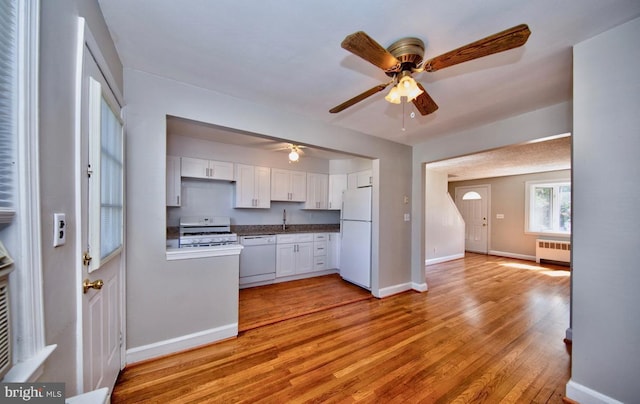 kitchen with white appliances, radiator, white cabinets, sink, and light hardwood / wood-style floors