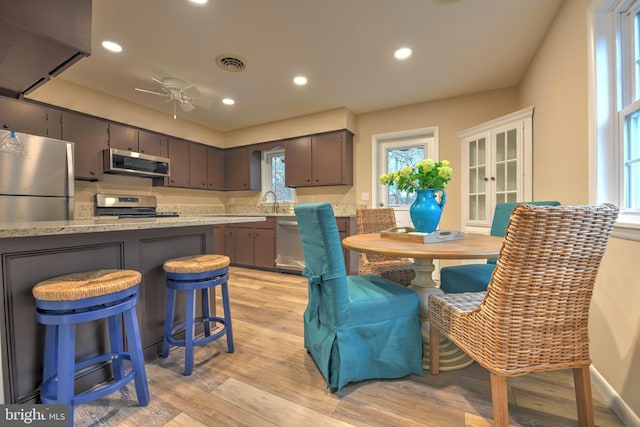 kitchen featuring ceiling fan, appliances with stainless steel finishes, dark brown cabinets, kitchen peninsula, and light wood-type flooring