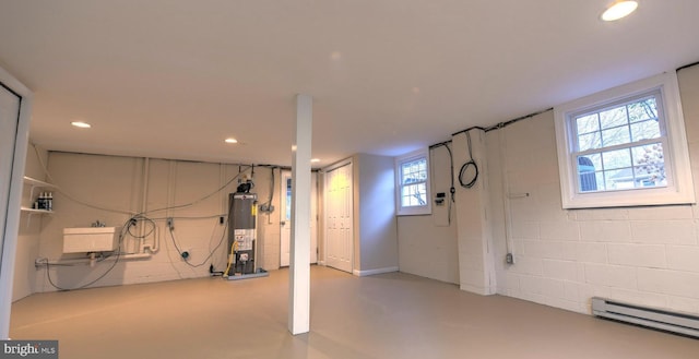 basement featuring a baseboard radiator, plenty of natural light, and water heater