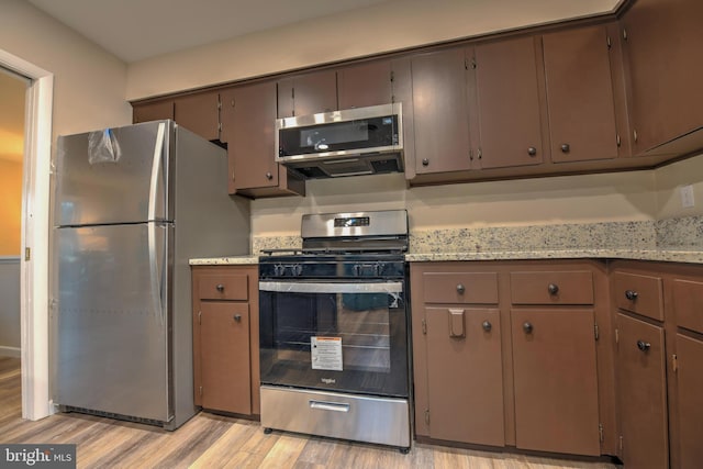 kitchen featuring dark brown cabinetry, light stone counters, light hardwood / wood-style flooring, and stainless steel appliances