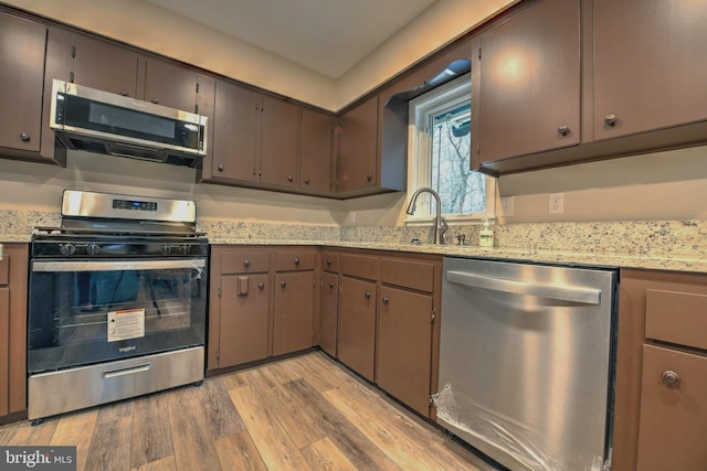 kitchen featuring sink, appliances with stainless steel finishes, dark brown cabinetry, light hardwood / wood-style floors, and light stone countertops