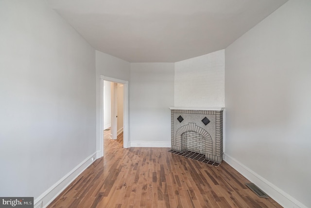 unfurnished living room with wood-type flooring and a brick fireplace