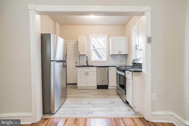 kitchen with white cabinetry, sink, stainless steel appliances, light hardwood / wood-style flooring, and backsplash