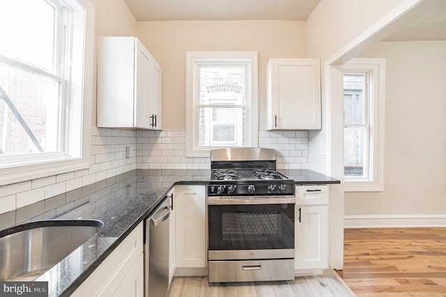 kitchen with dark stone counters, white cabinets, light hardwood / wood-style floors, and appliances with stainless steel finishes