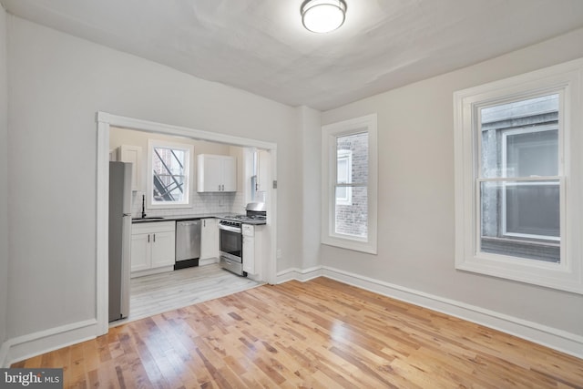 kitchen featuring sink, tasteful backsplash, light hardwood / wood-style floors, white cabinetry, and stainless steel appliances